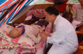 Dr. Li visits with patient whose house was destroyed and is now living under a tent.